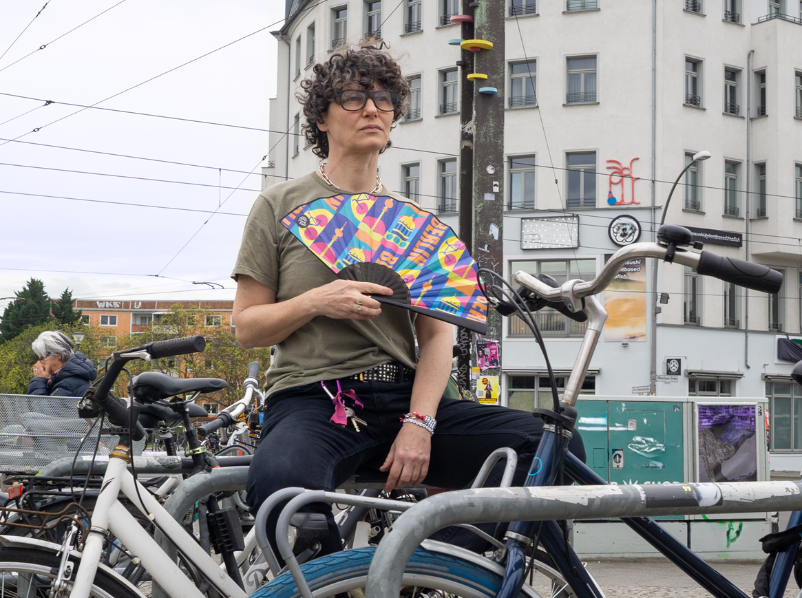 Frau sitzt zwischen Fahrrädern mit Fächer Berlin & bike in der Hand