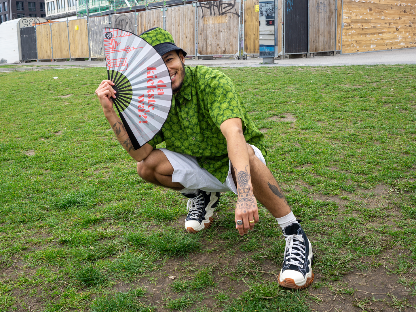 Person hält einen Fächer von I'm a Fan! mit Design "da kiekste wa!?" halb über das Gesicht und lächelt in die Kamera