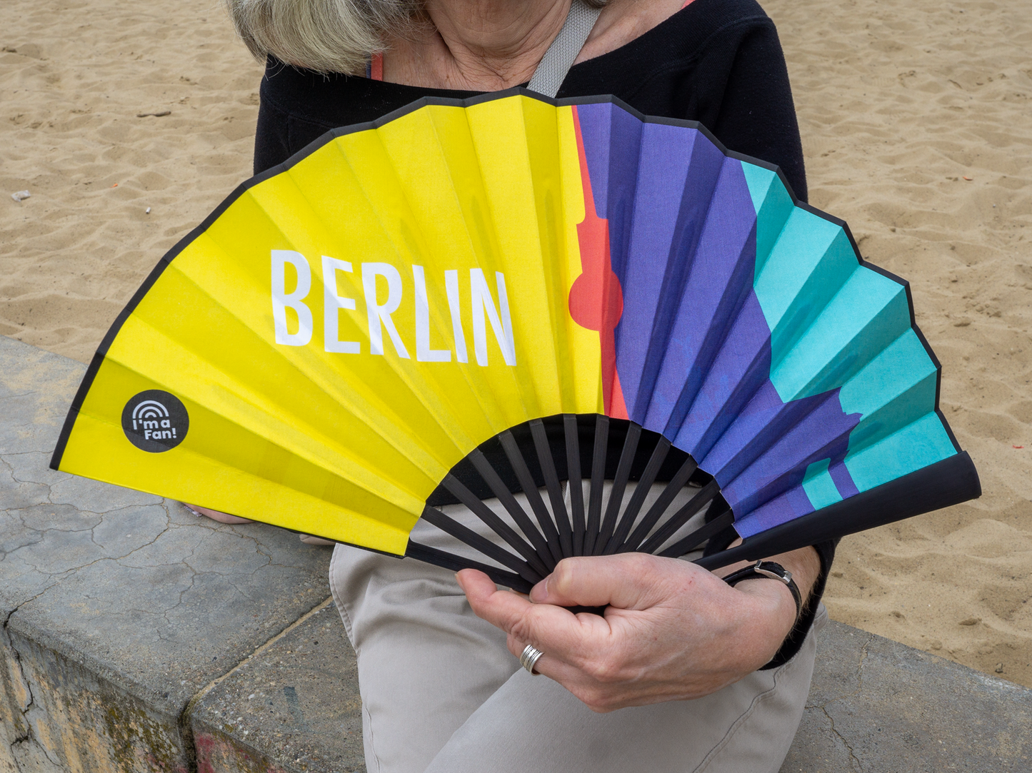Frau hält Fächer Berliner Wahrzeichen in der Hand, sitzend am Strand