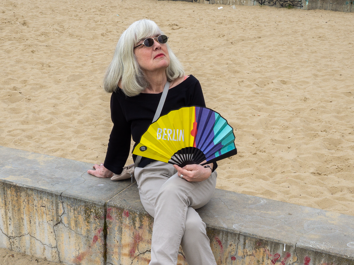Frau hält Fächer Berliner Wahrzeichen in der Hand, sitzend am Strand