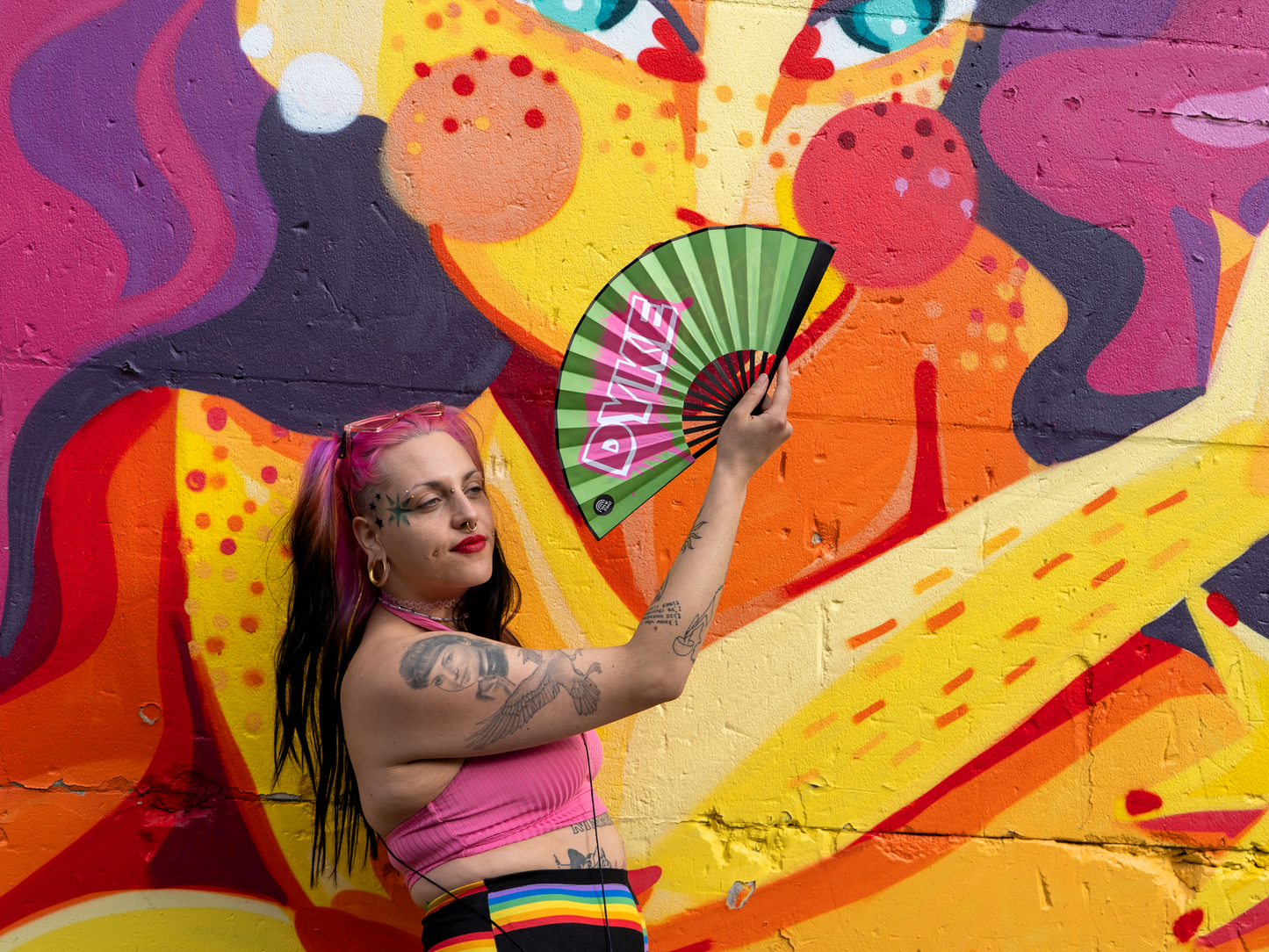 Fächer mit Design "DYKE" von I'm a Fan! gehalten von einer Person vor Graffiti Wand