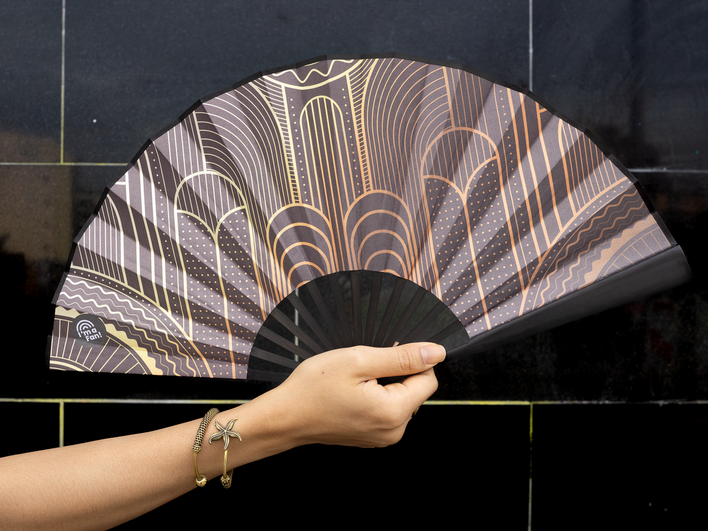 Großaufnahme des Fächers Design "Babylon" in der Hand einer Person vor schwarzer Wand