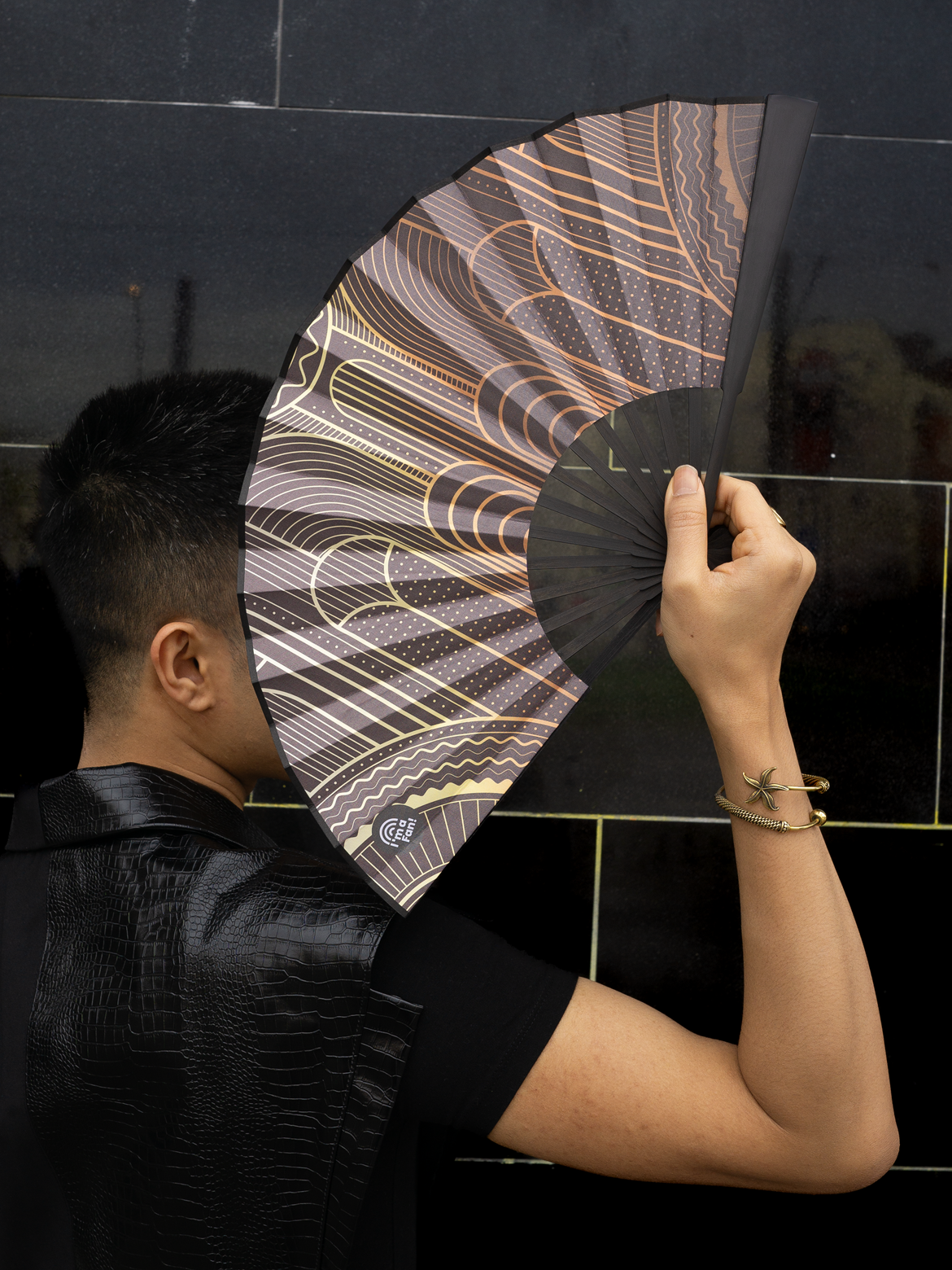 jemand hält den Handfächer "Babylon" seitlich und verdeckt damit das eigene Gesicht stylish vor schwarzem Hintergrund.